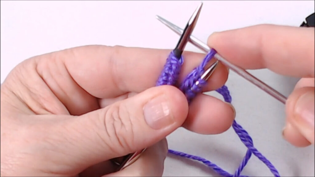 needles close up pulling a stitch onto the left needle